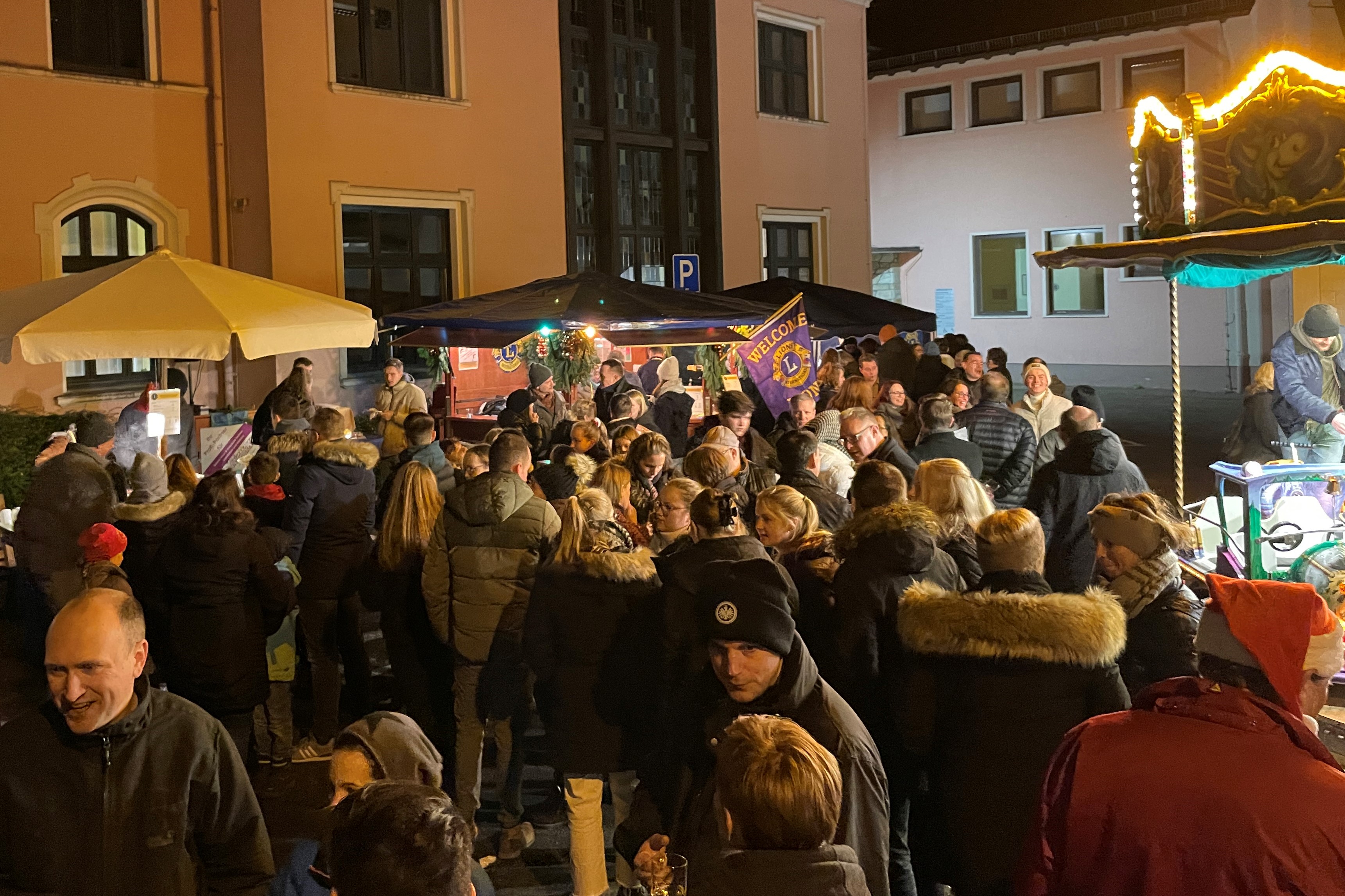 Viele Weihnachtsmarktbesucher stehen am Abend vor dem Lions Stand